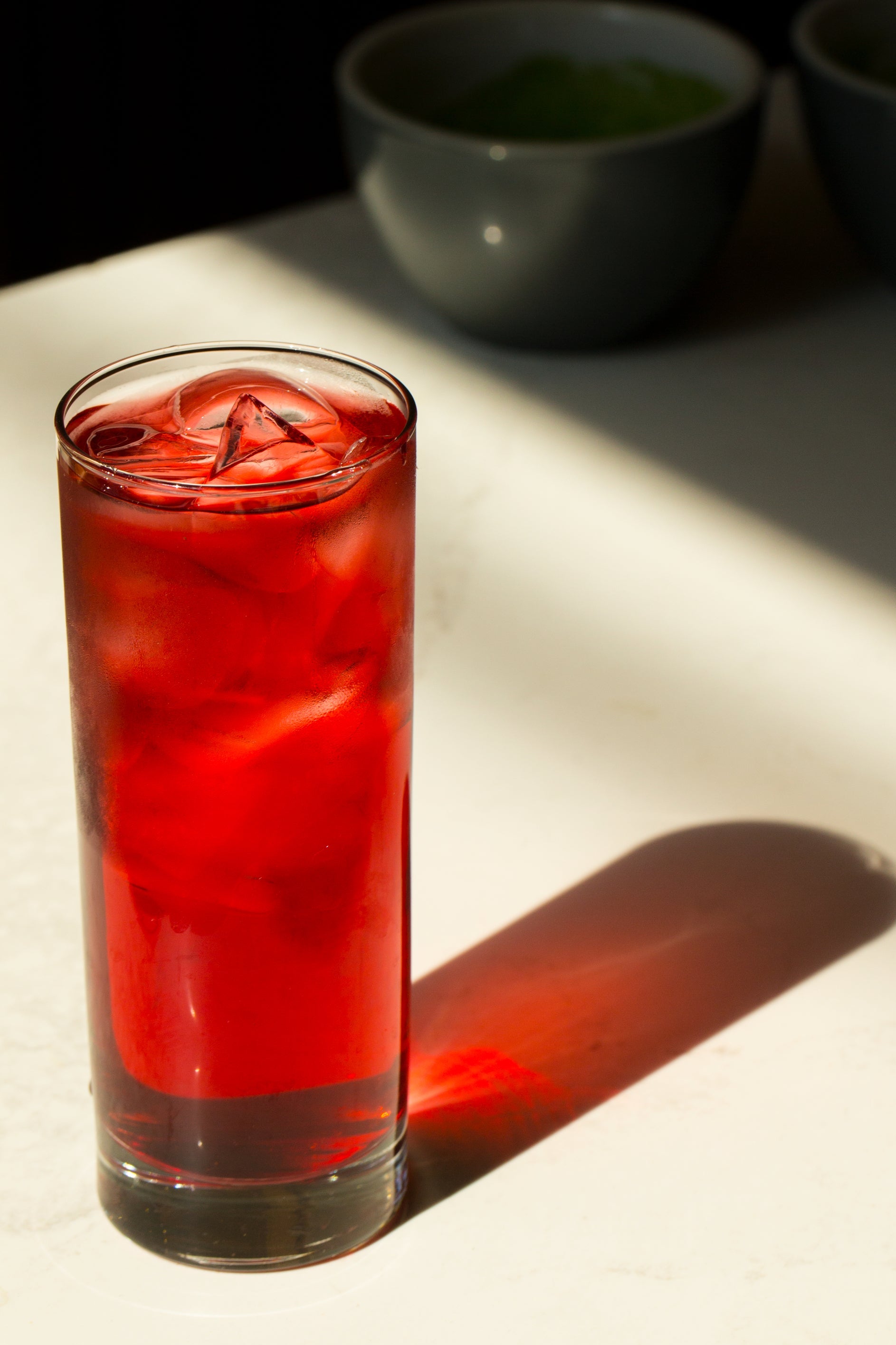 Red drink in a glass with ice cubes on a light surface
